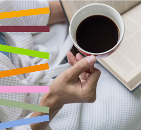 A person sat with a book on their lap holding a cup of coffee