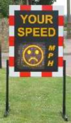 A Speed Indicator Device (SID): a board with a red and white striped border with the words 'Your speed' and small LED screen displaying an unhappy face.