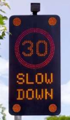 A Vehicle Activated Sign (VAS): an LED screen mounted to a pole displaying '30' in a red circle and the words 'slow down'.