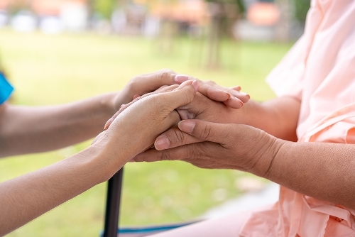 A close up photo of two people holding hands. The person on the right is in a wheelchair.