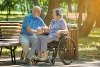 An elderly couple sat in a park. The woman is in a wheel chair.